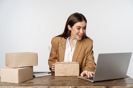 微笑快乐的女商人在办公室运送包裹，在笔记本电脑网站上处理订单，向客户发送货物，白色背景