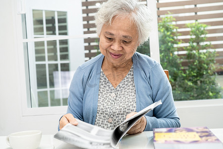 亚洲老年或老年老妇患者坐在护理医院病房的床上看书，健康强大的医疗理念。