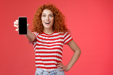 欢快迷人的魅力欧洲红发女孩卷曲发型展示智能手机屏幕微笑快乐推广应用程序建议推荐良好的应用程序社交媒体页面红色背景