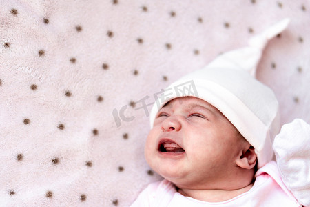 女孩肚子疼摄影照片_童年、疾病、绞痛、腹胀、母性、健康概念 — 戴着帽子、焦躁不安、忧心忡忡、悲伤的新生女婴睡着时哭着尖叫，肚子疼，躺在床上，张着嘴