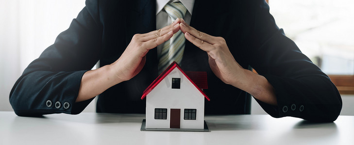一个灰色的小样板房是一个住房项目中的房屋示例，保险销售人员正在房屋保险中进行象征性的房屋保护行为。