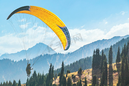 黄色扁平化摄影照片_黄色滑翔伞，在风景如画的山脉背景下，空中有滑翔伞