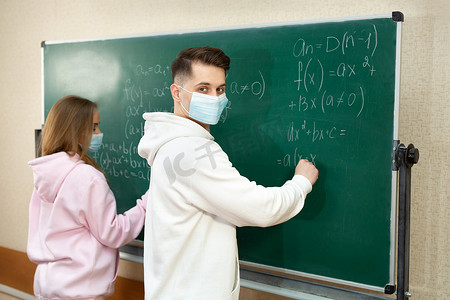 大流行期间，一群戴着口罩的学生在教室的黑板上写字。