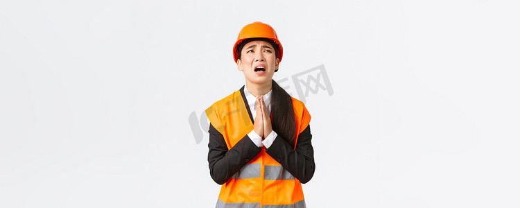 绝望而鲁莽的亚洲女建筑经理、建筑师恳求上帝、戴着安全帽、手牵着手祈祷、恳求、请求上帝帮助、在白色背景中乞讨