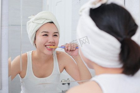 年轻的亚洲女人对着镜子刷牙。