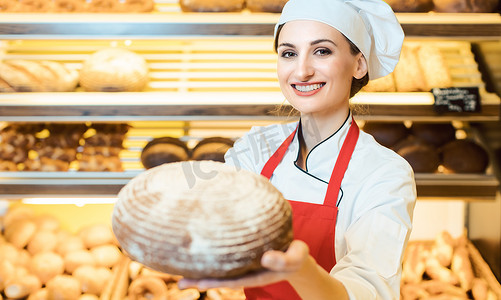 穿着围裙的女售货员在面包店里展示新鲜面包