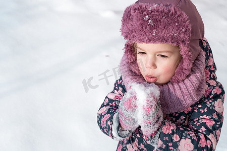 保暖显瘦摄影照片_冬天、游戏、家庭、童年概念 — 特写肖像正宗的学龄前未成年 3-4 岁女孩，穿着粉色帽子保暖衣服，在冰雪天气里微笑着。