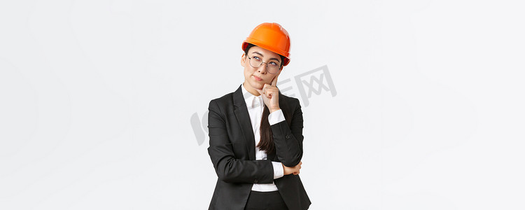 佩戴安全帽摄影照片_体贴的创意亚洲女首席建筑师、建筑工程师思考、佩戴安全帽和西装、思考建筑的最佳选择、站立白色背景