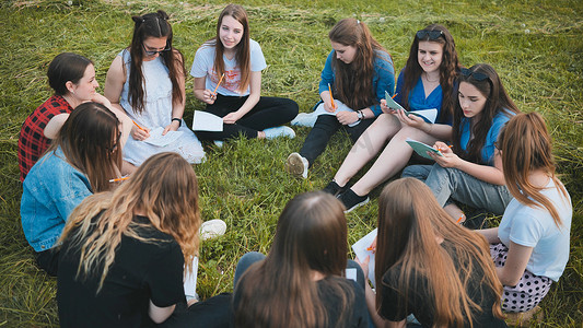 一群女学生在草地上围坐成一圈，拿着笔记本集体作业。