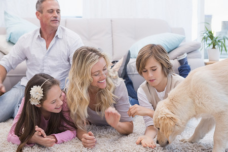 微笑的家庭与他们的宠物黄色拉布拉多在地毯上