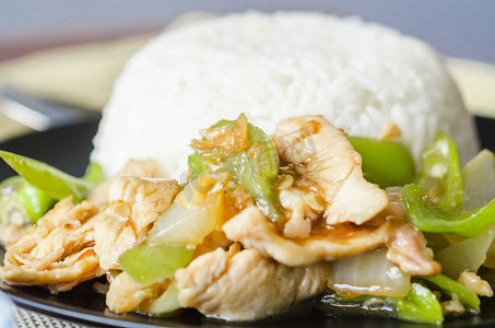 米饭炒菜摄影照片_鸡肉与青辣椒和蒸米饭在黑盘中炒。