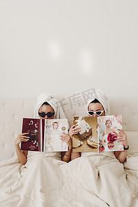 上午摄影照片_两个戴着太阳镜的女孩，床上有杂志。