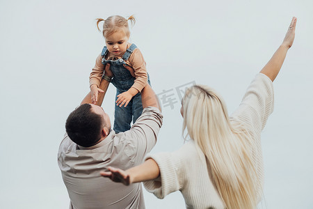 年轻的家庭在户外玩得很开心，父亲将小女儿抱在头上，母亲模仿飞机