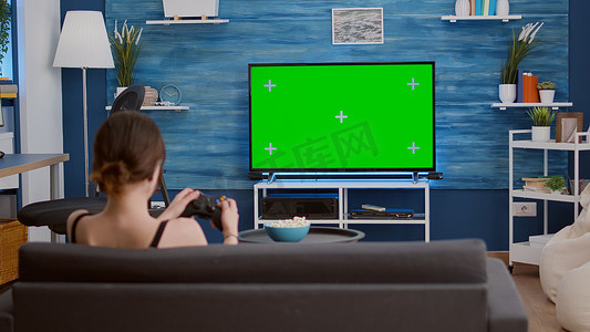 游戏钥匙摄影照片_游戏玩家女孩在绿屏电视上用无线控制器玩控制台视频游戏，在沙发上放松