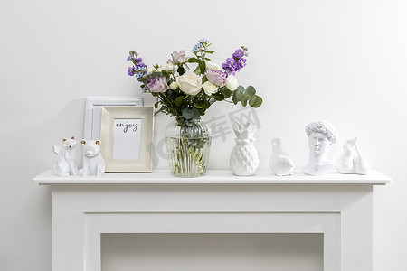 蓝色花束摄影照片_白色咖啡桌上放着玻璃花瓶里的哈克利亚绒毛、紫色和白色玫瑰、小茶玫瑰、马蒂奥拉·印加纳和蓝色鸢尾的花束。