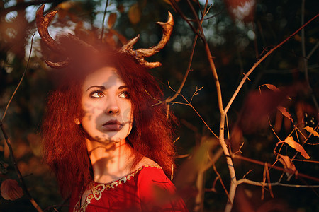 秋季森林中穿着红色长裙、有鹿角的女人。