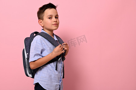 背着书包的学生摄影照片_一个背着书包的男学生的侧面肖像，粉色背景，有复印空间。