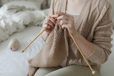 妇女的双手用米色羊毛纱线编织。