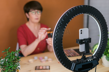 时影摄影照片_中年妇女在录制视频时谈论化妆品，包括眼影、腮红调色板和刷子。
