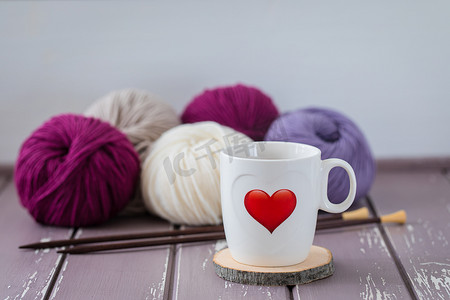 白色的茶，在彩色纱线和织针的背景下，有一颗红色印刷的心。