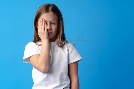 小女孩在工作室的蓝色背景下哭泣。