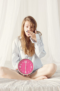 女孩坐在床上，床上有粉红色的大钟。