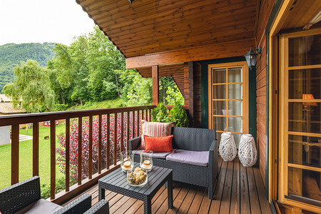阴天的夏日，乡村的木制小屋内配有桌子和沙发的舒适露台，周围环绕着绿树和树木