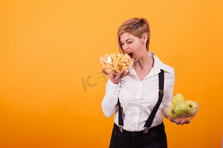 可爱的泡芙摄影照片_有魅力的年轻女子在黄色背景下看着那些美味的玉米泡芙。
