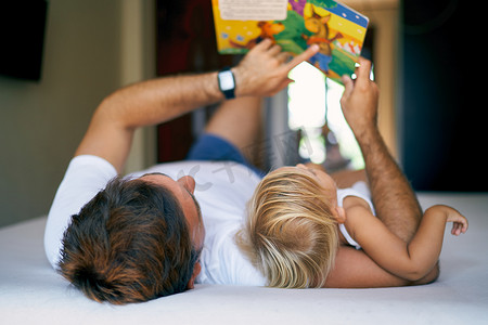 爸爸给女儿看床上放着一本有图片的书