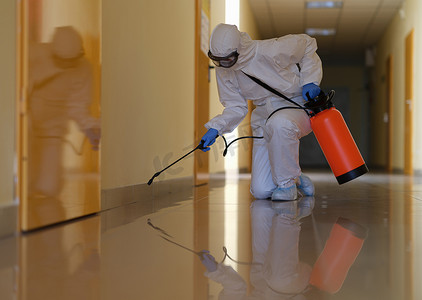 打扫卫生的摄影照片_穿着防护服的人员对办公室和走廊进行消毒，以防止 COVID-19 传播