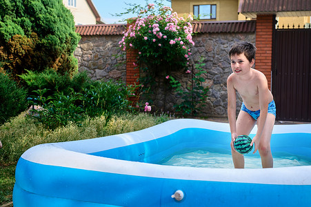 夏日阳光明媚的日子，英俊的白人学龄男孩在充气泳池里游泳时玩浮球
