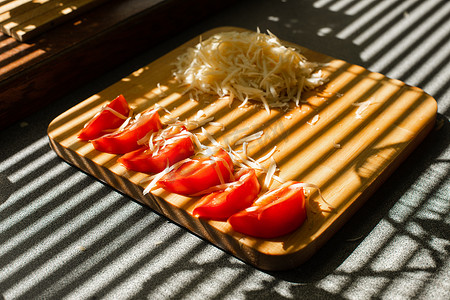 厨房的木板上放着一小堆磨碎的新鲜奶酪和红西红柿
