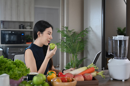 素食妇女在家庭厨房制作绿色蔬菜冰沙时，在数字平板电脑上阅读食谱。