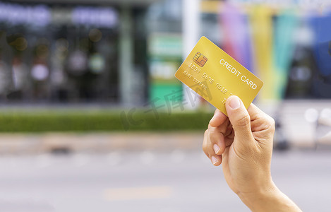 妇女手持金信用卡会员卡在模糊的百货商店背景。