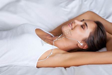 音乐逃亡......一个美丽的年轻女子躺在床上听音乐的肖像。