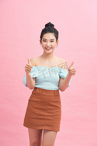 漂亮的亚洲女人站在粉红色的背景上微笑着，用拇指做“好”信号