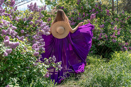 丁香花中的时装模特，穿着美丽长裙的年轻女子在风中飘扬，盛开的花园中的户外美女肖像