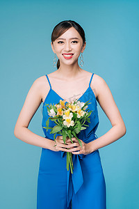 蓝色背景中身着蓝色裙子、手捧鲜花的漂亮亚洲女性