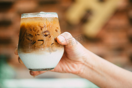 玻璃杯子摄影照片_手拿冰拿铁咖啡放在底部有奶油的玻璃杯中。