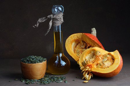 静物画，由两半南瓜装饰瓶中的葵花籽油组成，并躺在深色背景的桌子上的干带壳炸黑南瓜籽周围