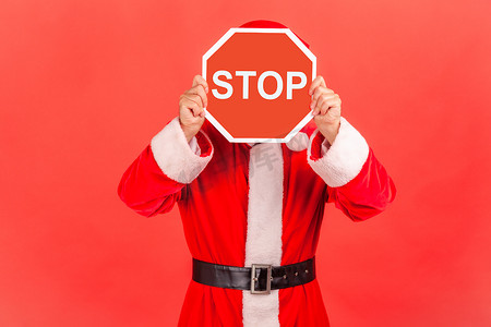 穿着圣诞老人服装的未知男子用停止符号遮住脸，匿名者举着红色交通标志，警告走，禁止概念。