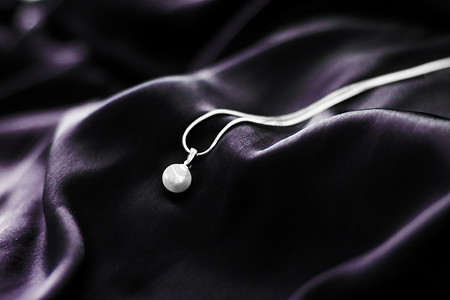 丝绸珠宝摄影照片_深紫色丝绸背景的豪华白金珍珠项链，节日魅力珠宝礼物