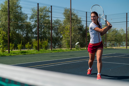 女性热摄影照片_炎热的夏日，年轻的白人女子在室外球场打网球。