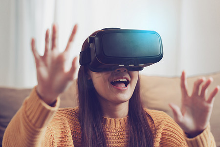令人兴奋的亚洲女性戴着可穿戴 VR 耳机在家里的客厅里在线玩体育游戏。