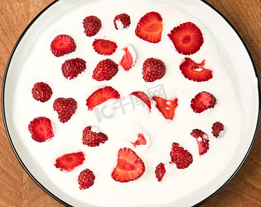 美味多汁的红草莓片埋在乳制品、酸奶油中，埋在木板上的白盘里，