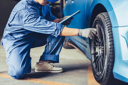 亚洲汽车修理师拿着剪贴板，并根据客户索赔订单在汽车修理店车库检查维修车辆。