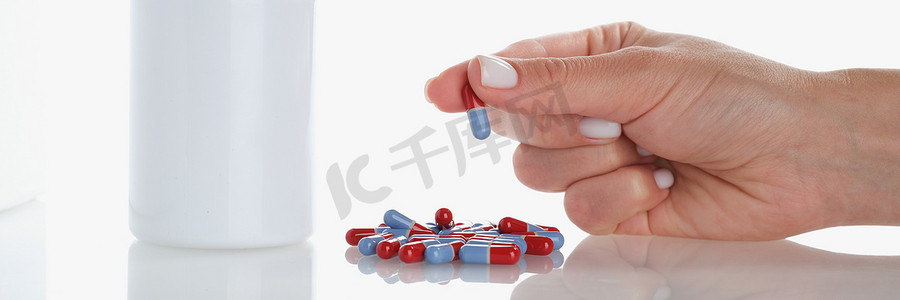 女人的手握着一颗果冻胶囊，一堆散落在表面的药丸