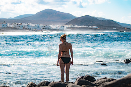 西班牙加那利群岛拉圣兰萨罗特岛冲浪胜地野生石滩和海岸线的女游客。