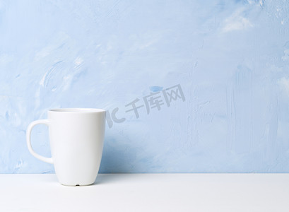 浅蓝色混凝土墙对面的白色桌子上放着白色杯子，上面放着茶或咖啡。