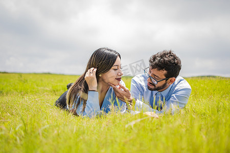 一对情侣躺在草地上互相看着对方，热恋中的年轻情侣躺在草地上互相抚摸着对方的脸，两个相爱的人躺在草地上互相看着对方